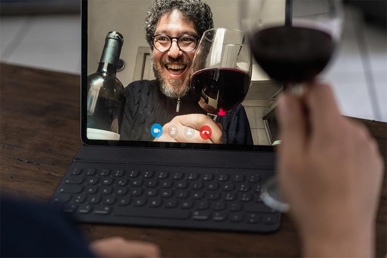 Two older adult friends toasting with red wine while video chatting