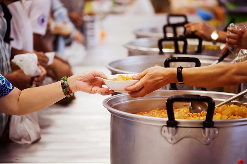 Closeup on the hands of a volunteer passing over a bowl of food in a soup kitchen