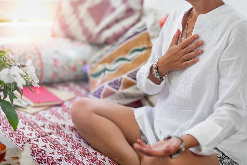 A yoga participant sitting cross-legged on a patterned mat with one had upturned on their lap and the other on their chest