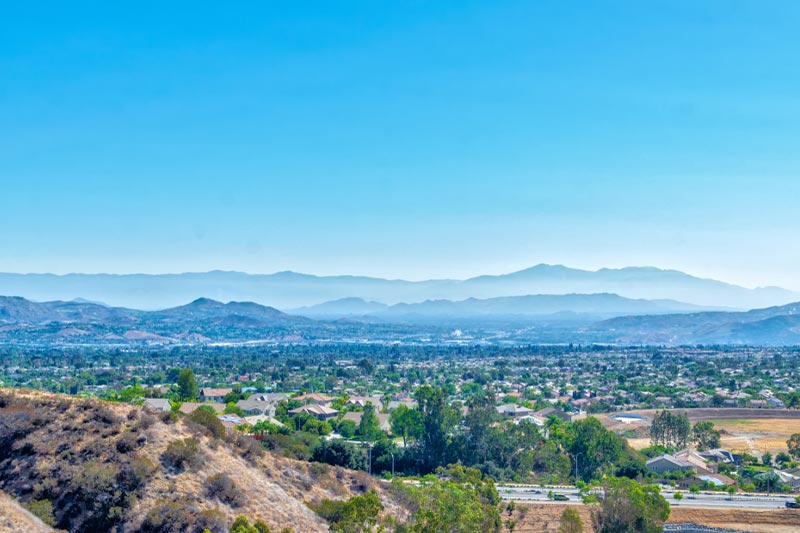 Southern California houses below in Inland Empire on hot summer morning with mountains in the distance.