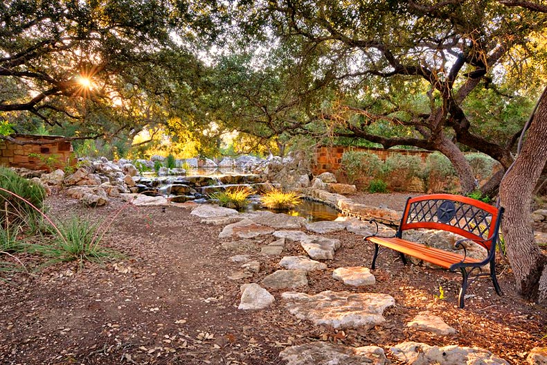 A small pond, park bench, and stone pathway located in Hill Country Retreat of San Antonio, Texas
