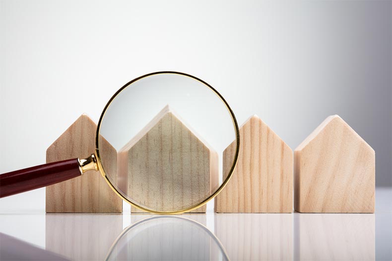 A magnifying glass in front of wooden house silhouettes arranged in a row