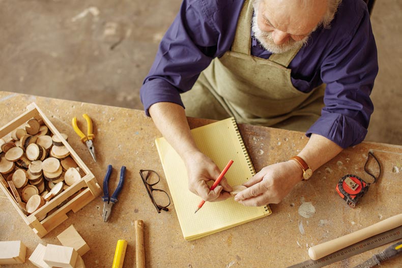 Top view of a senior man taking measurements with a pencil and notebook while woodworking