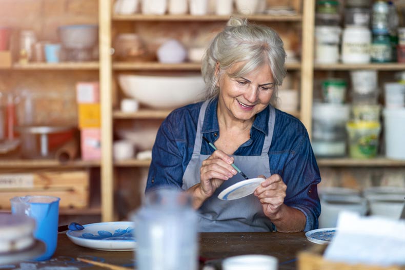 A senior craftswoman painting a clay plate in an art studio