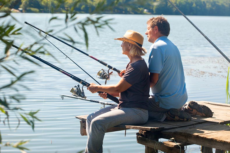 An older couple sitting on the end of a dock and fishing