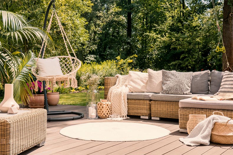 A terrace with a leisure sofa, a table, and a swing in the green garden of a vacation home.