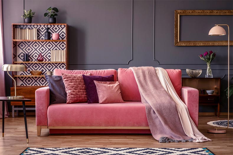 A pink sofa with pillows and a blanket and a vintage cupboard in the background