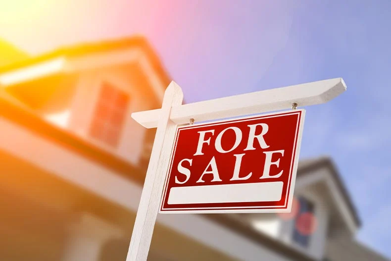 Image of a for sale sign taken from a low angle with a home in the background