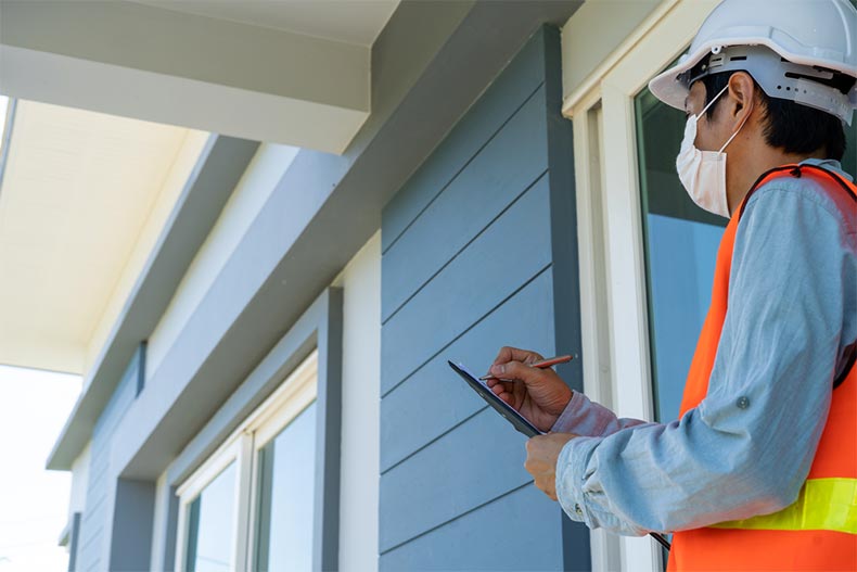 An inspector in a reflective vest taking notes with a clipboard at a new construction house