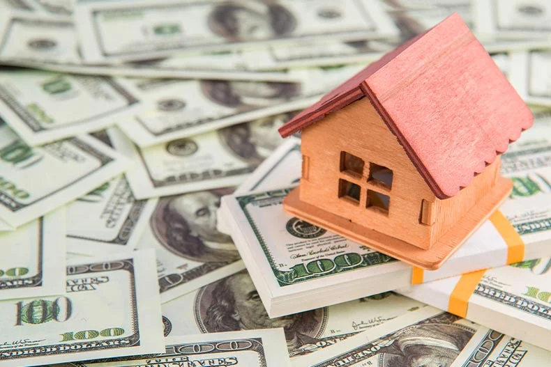 Picture of a small toy home on top of a pile of of $100 bills