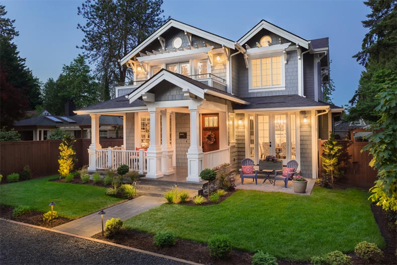 Exterior view at night of a new home with a green lawn, a covered porch, and stately gables and columns