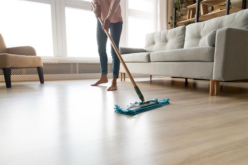 A barefoot woman cleaning wooden laminate flooring using a microfiber mop pad