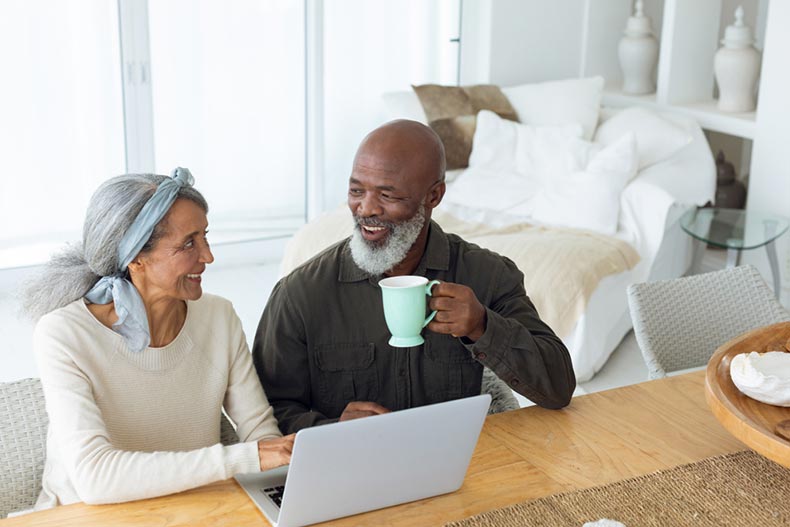 A senior couple smiling at each other while using a laptop to shop for homes