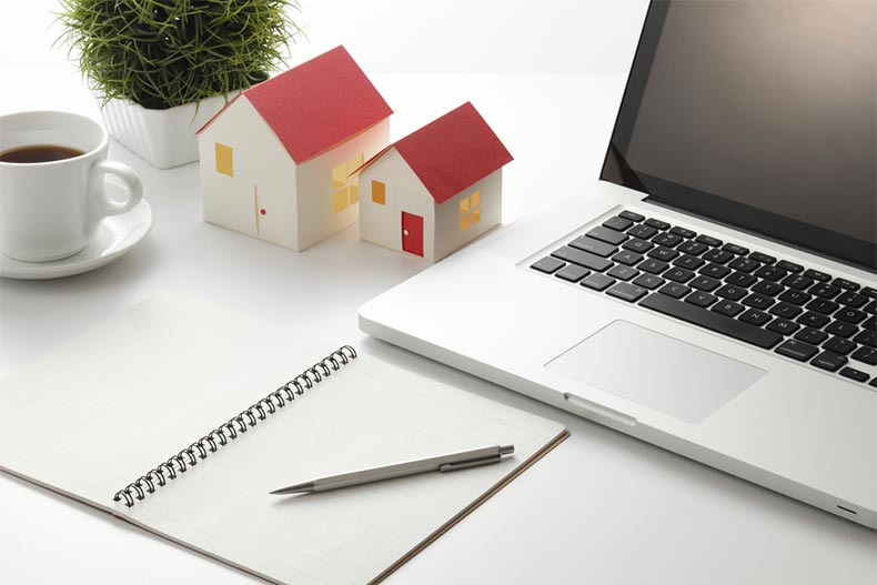 Two tiny model homes beside a laptop and a notebook with a pen