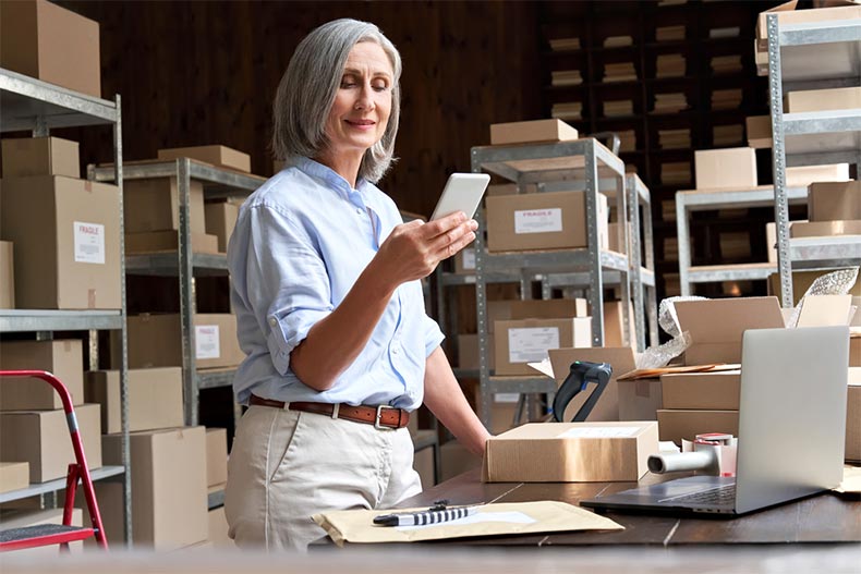 An older woman working in a warehouse and using a mobile app to check a parcel box