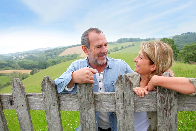 A smiling active adult couple leaning on fence in the countryside