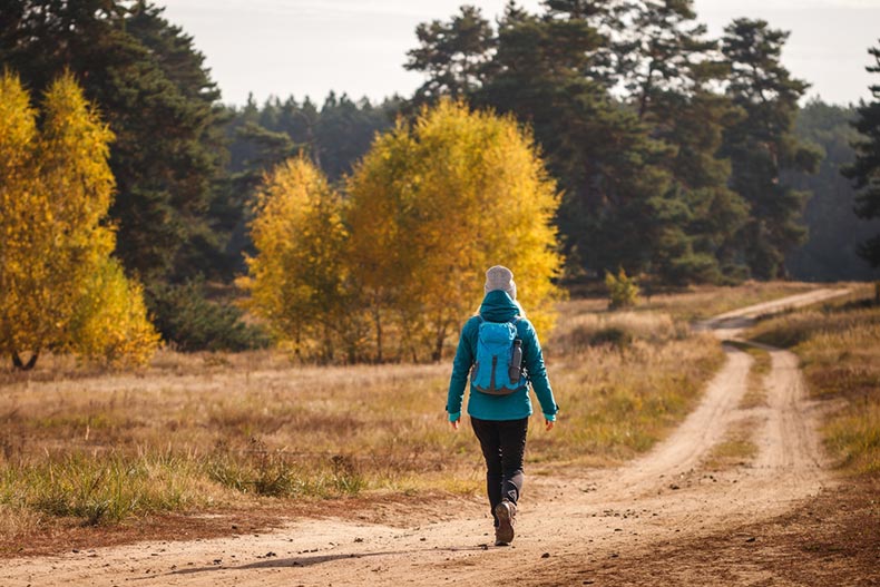 An older woman hiking on a trail in an autumn forrest near the 55+ community she lives in