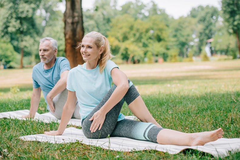 An older man and woman practicing yoga while sitting on yoga mats in a park