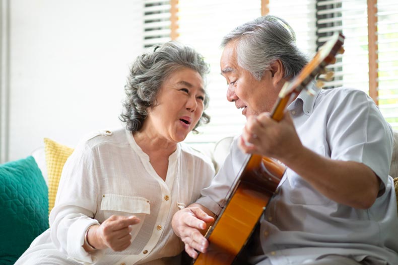 A senior couple sitting on a couch while singing and playing acoustic guitar together