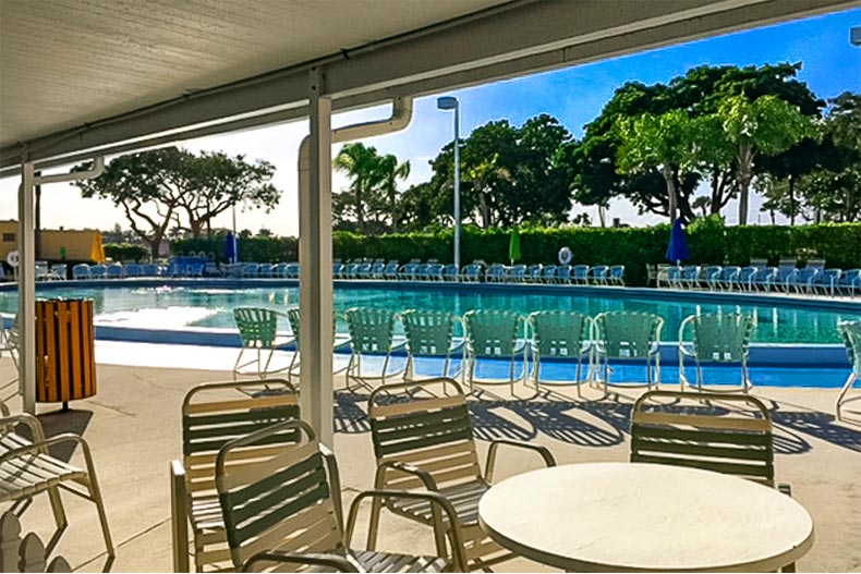 Patio chair surrounding a table with more in the background surrounding a pool, located in Kings Point in Delray Beach, Florida