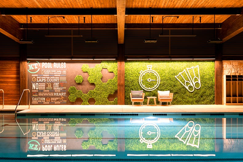 Pool rules and a plant mural next to an indoor lap pool in Kissing Tree, located in San Marcos, Texas