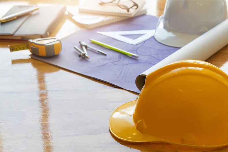 Blueprints, hard hats, and tools on a wooden table