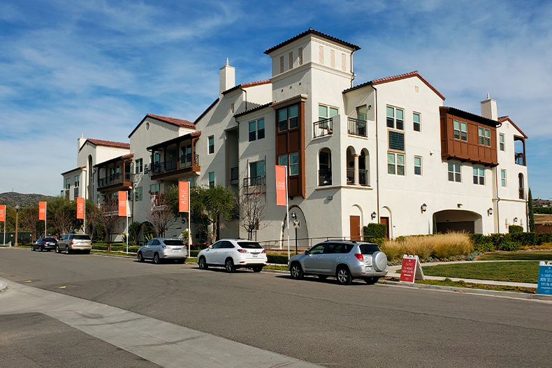 Exterior view of a condo building in Buena Vida at La Floresta next to a street lined with cars and street lights, located in Brea, California