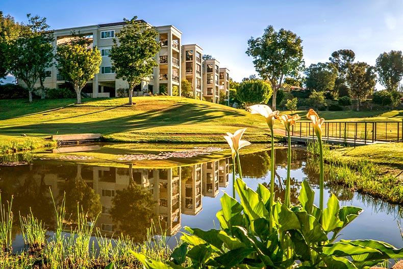 Exterior view of condo buildings in Laguna Woods Village with a pond and white lilies in the foreground