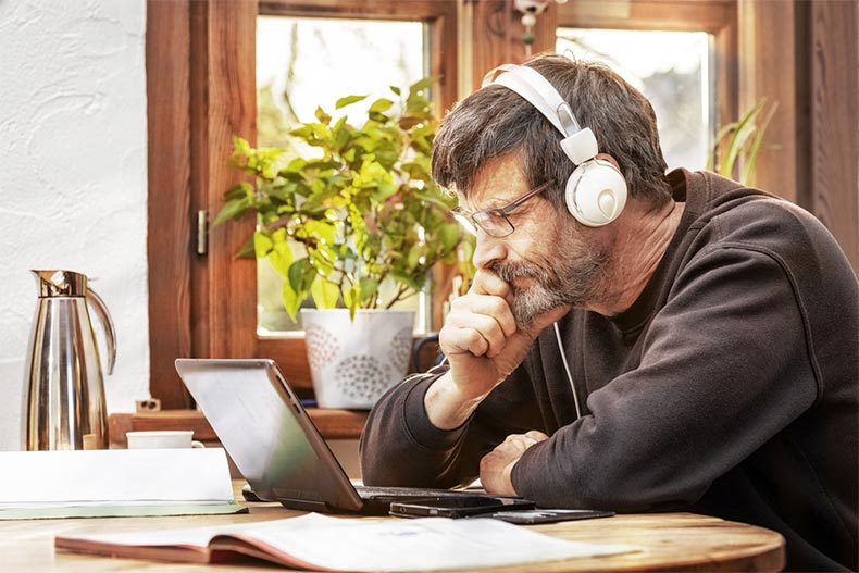 An older man with headphones on concentrating as he listens to an online lesson