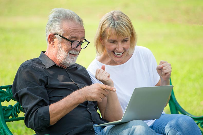 An active adult couple browsing homes for sale on a laptop while sitting on a park bench