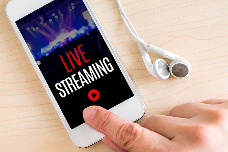 Closeup on a hand pressing the play button on a smart phone livestreaming a concert