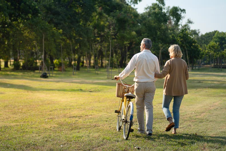 A mature couple walking a bicycle through a field in a 55+ community