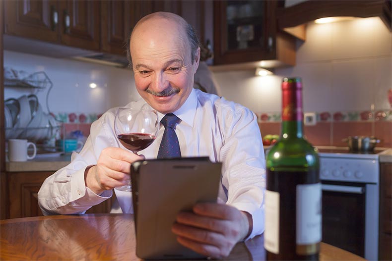 An elderly man in a shirt and tie toasting with a glass of wine via video chat