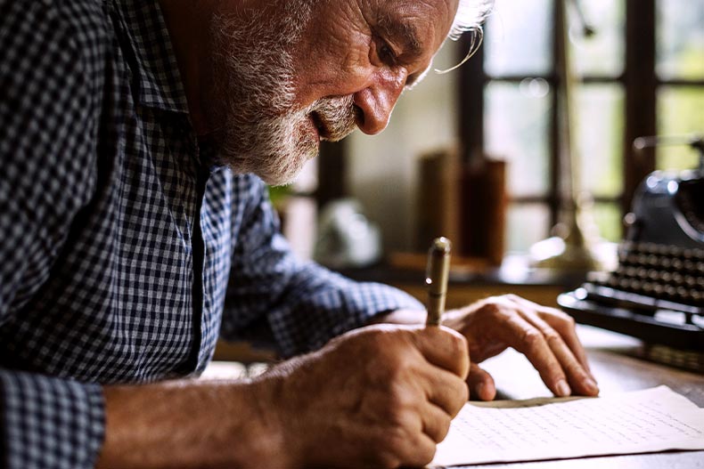 Closeup of a senior man with a white beard writing a letter
