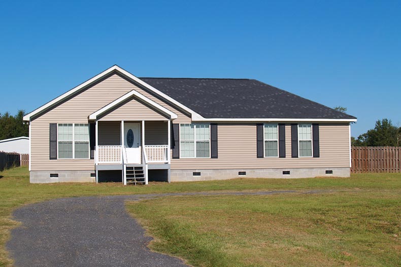 View of a small manufactured home with a covered porch and vinyl siding