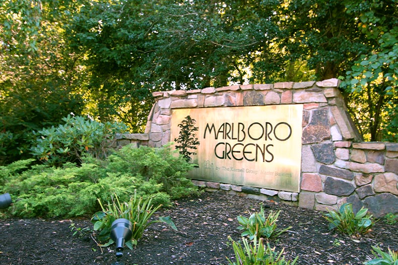  The stone and bronze community sign for Marlboro Greens surrounded by greenery, located in Englishtown, New Jersey