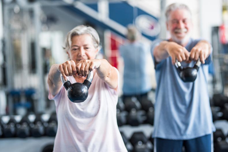 Two 55+ adults work out with dumbbells as part of their fitness center exercise routine