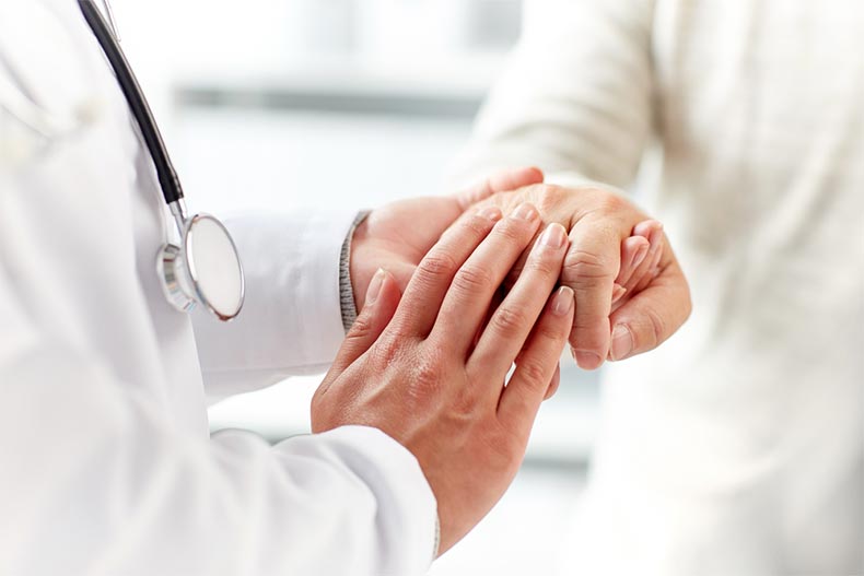 Close up of doctor holding the hand of a senior man at a hospital