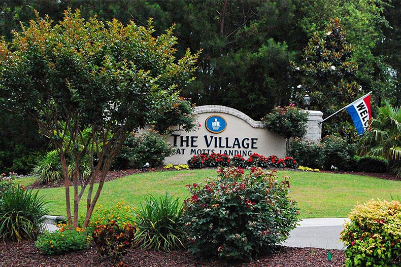 The entrance sign at The Village at Motts Landing with a welcome flag, located in Wilmington, North Carolina