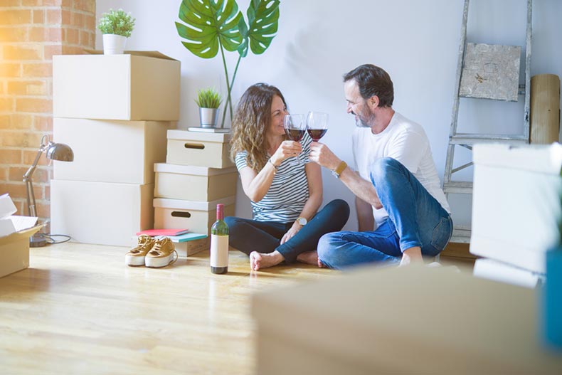 An active adult couple drinking wine while surrounded by moving boxes