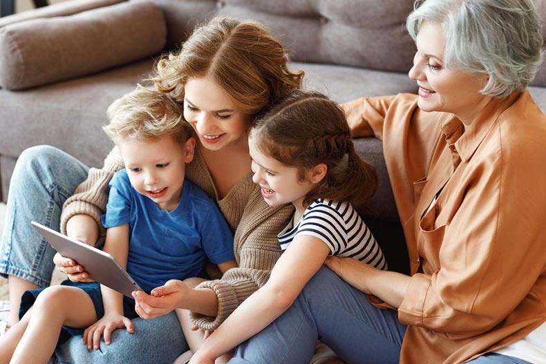 A mother and grandmother sitting on the floor and browsing a tablet with kids in a cozy living room