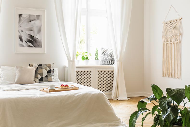 A white bed in a bright and peaceful bedroom with plants on a window sill seat