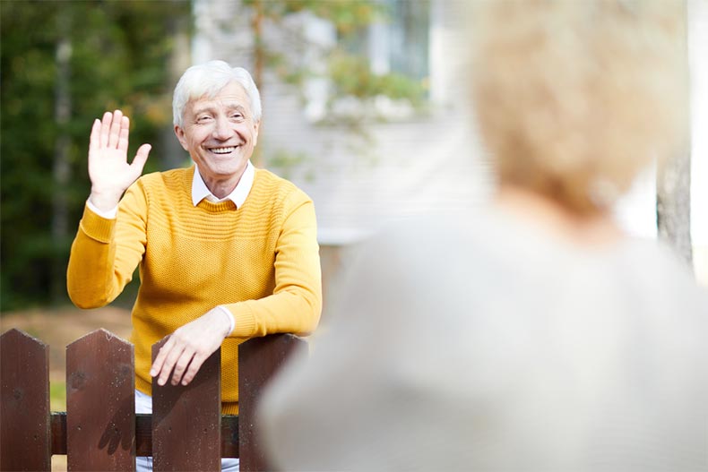 Friendly, older man waving to his neighbor while standing by a fence