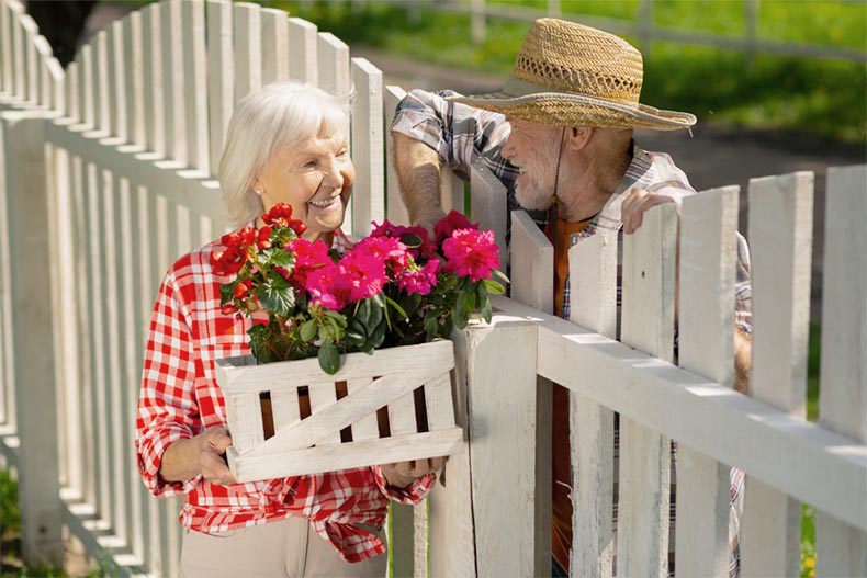 An older woman with flowers talking to an older man over a fence