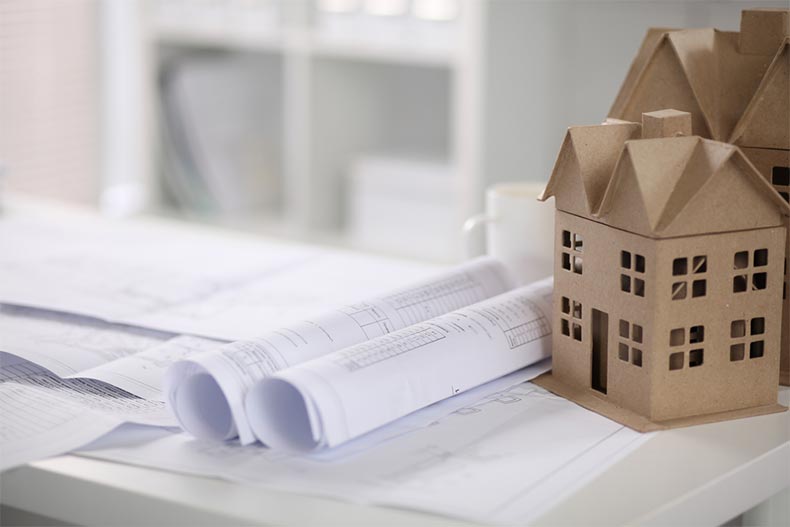 Blueprints for a new construction home rolled up beside a paper model of a house