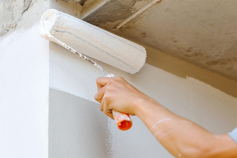 Closeup on a hand with a paint roller painting a wall white