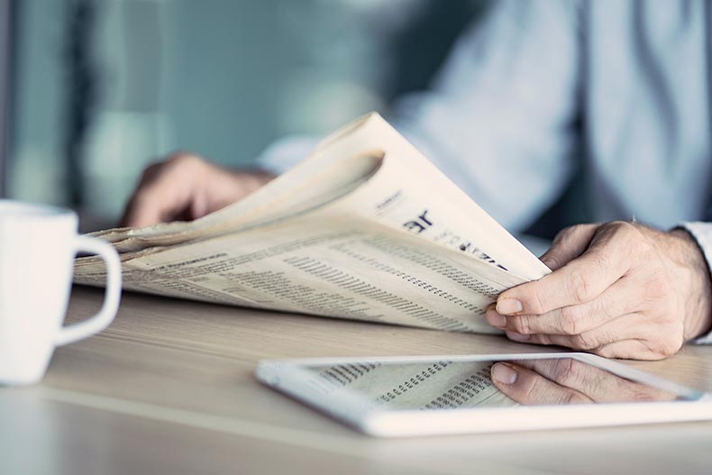 Closeup of the hands of a businessman reading the newspaper at a table