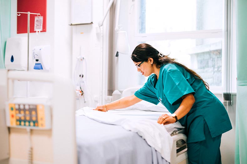 A nurse in blue scrubs fixing a hospital bed