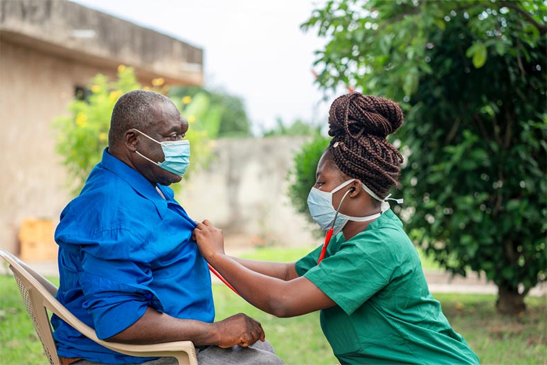 A nurse taking care of an old man while he sits outside at a nursing home