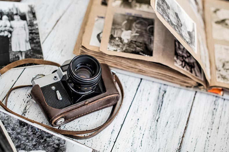 An old film camera and a family album on a white, wooden background